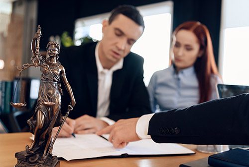 Divorce lawyer discussing paperwork with a man and woman with a law statue on the table